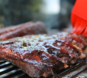 What Makes Good Southern BBQ? ribs on a grill with a brush putting on bbq sauce